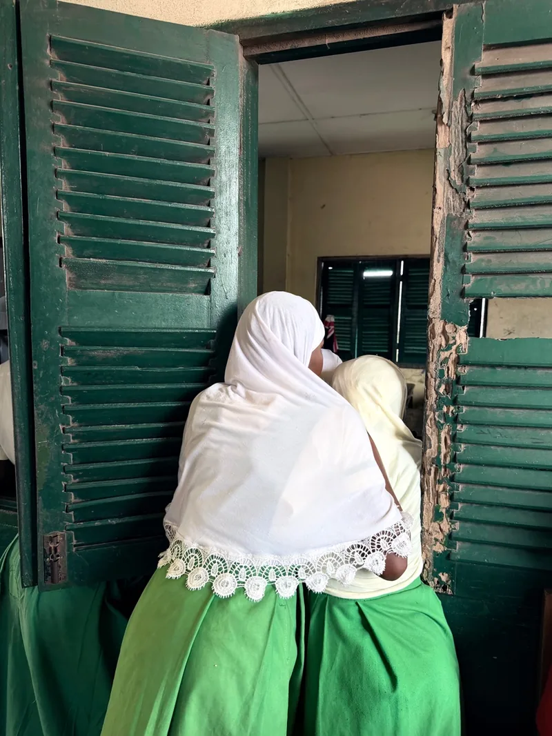 Students entering a classroom through green wooden shutters
